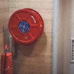 Red fire hose reel and extinguisher inside a building corner.