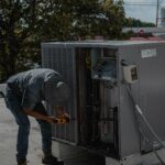 A technician is repairing an air conditioning unit on a rooftop, demonstrating skilled manual work.