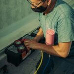 A technician kneels outdoors, performing HVAC maintenance using specialized tools, enhancing system performance.